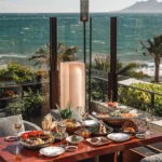 Terrace table laid with a spread of signature dishes and wine over a sea view at Zuma Cannes