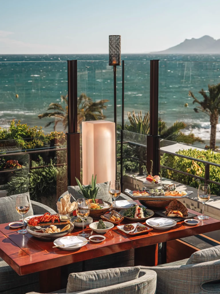 Terrace table laid with a spread of signature dishes and wine over a sea view at Zuma Cannes