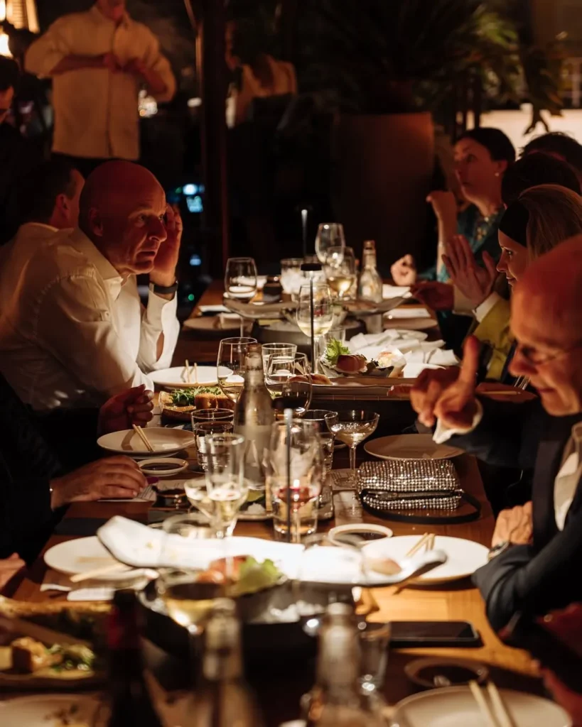 Guests seated along a long table over dinner and drinks at Zuma Cannes
