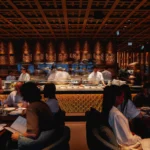 Diners seated in front of the open sushi kitchen under a latticed ceiling at Zuma Cannes