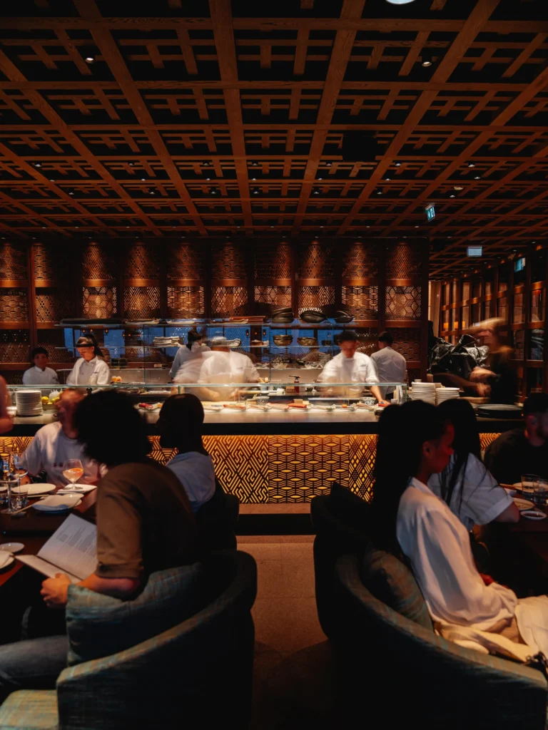 Diners seated in front of the open sushi kitchen under a latticed ceiling at Zuma Cannes
