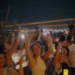 Guests dancing with raised hands and candlelight overlooking the bay at night at Zuma Cannes