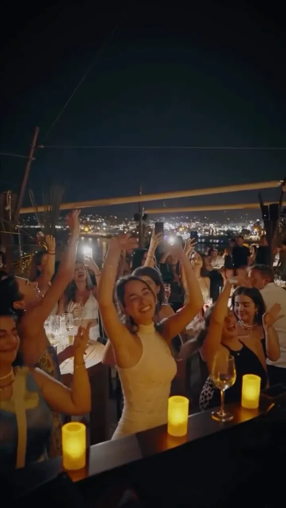 Guests dancing with raised hands and candlelight overlooking the bay at night at Zuma Cannes