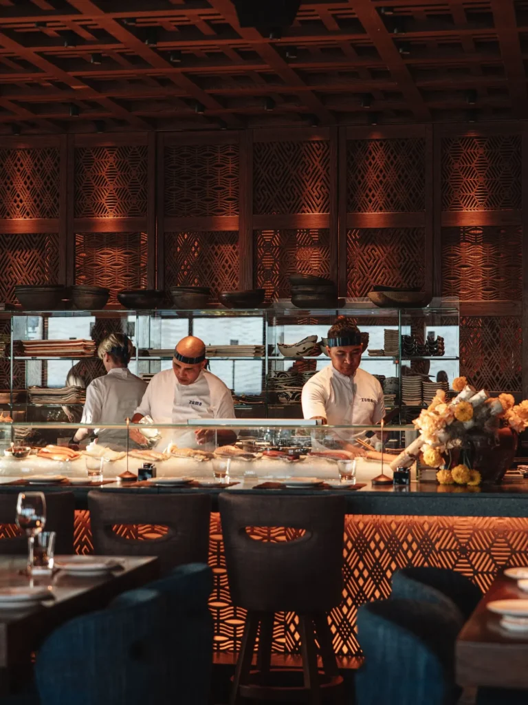Chefs in headbands working the sushi counter beneath latticed wood panelling at Zuma Cannes