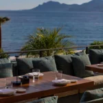 Cushioned terrace banquette and set table overlooking the sea and hills at Zuma Cannes