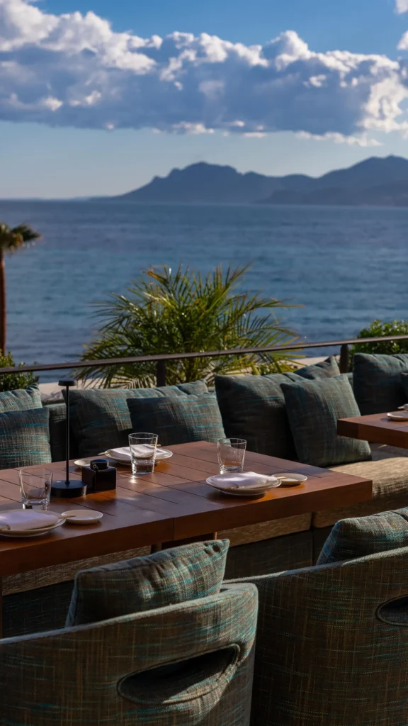 Cushioned terrace banquette and set table overlooking the sea and hills at Zuma Cannes