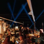 Guests dining on the terrace under sail canopies and blue beam lights at night at Zuma Cannes