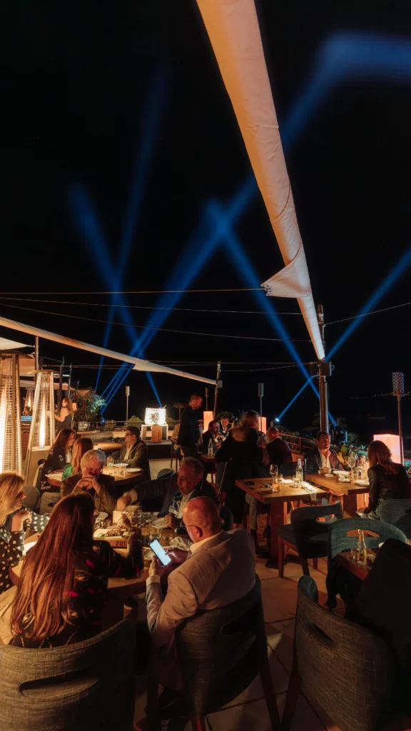 Guests dining on the terrace under sail canopies and blue beam lights at night at Zuma Cannes