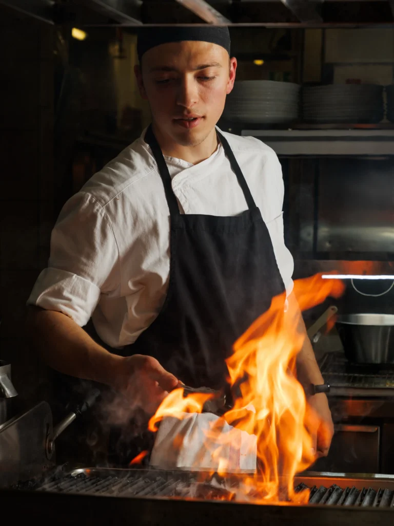 Chef grilling steak over an open flame at STK Milan