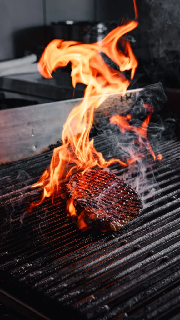Grilled steak cooking over an open flame at STK Milan