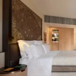 Elegant hotel bedroom with white linens, textured wall finishes and warm contemporary furnishings at Bulgari Hotel Milano