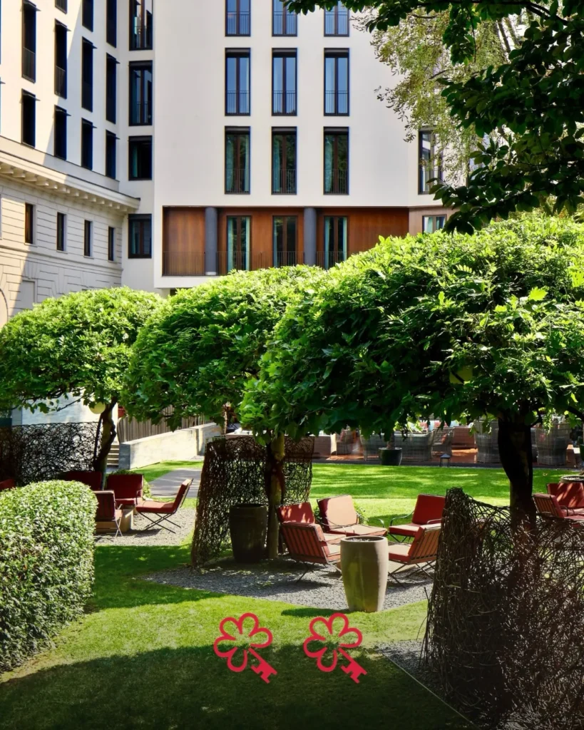 Lush green garden with manicured hedges, outdoor seating and the hotel facade at Bulgari Hotel Milano