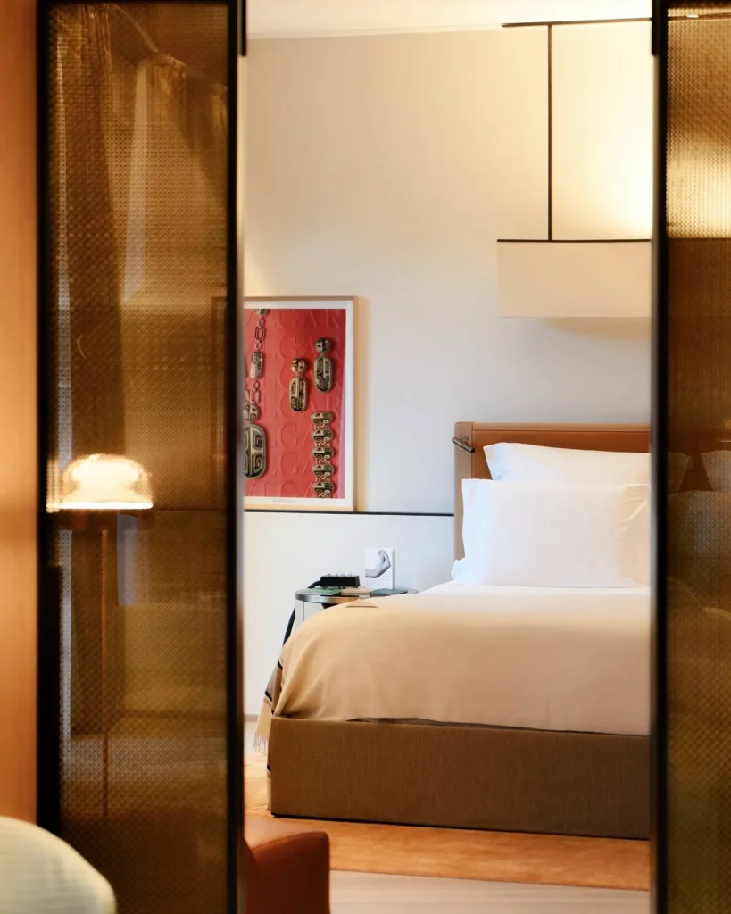 Luxury hotel bedroom with crisp white bedding, warm wood finishes and elegant contemporary furnishings at Bulgari Hotel Milano