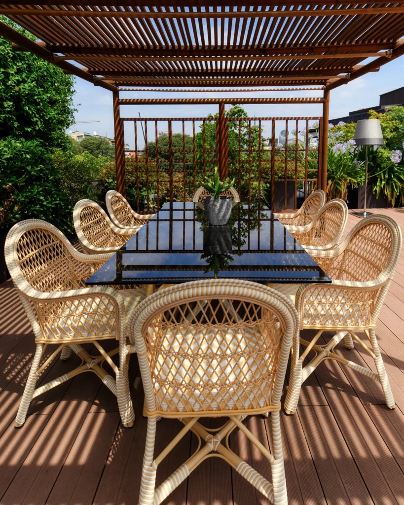 Outdoor dining terrace with woven chairs, a long table and a timber pergola at Bulgari Hotel Milano