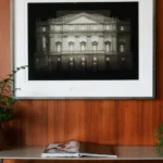 Framed artwork displayed above an upholstered chair against a warm wood-paneled wall in a Bulgari Hotel Milano suite