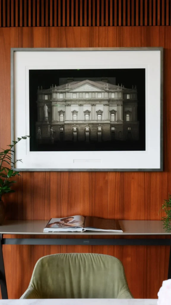 Framed artwork displayed above an upholstered chair against a warm wood-paneled wall in a Bulgari Hotel Milano suite