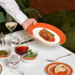 Chef presenting a colorful gourmet dish on an elegant restaurant table at a Bulgari hotel