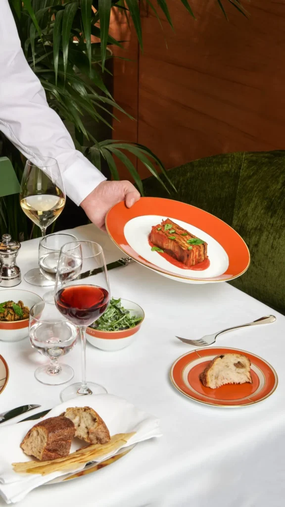 Chef presenting a colorful gourmet dish on an elegant restaurant table at a Bulgari hotel