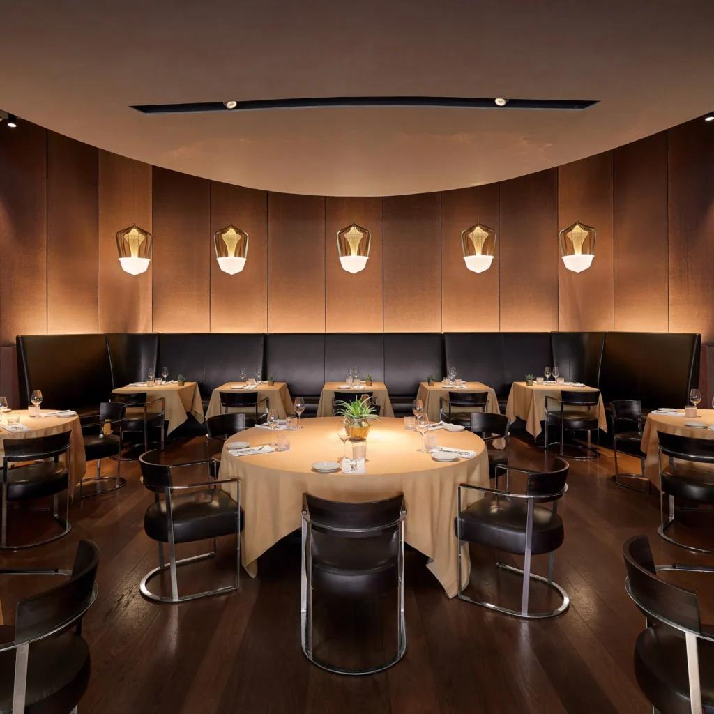 Elegant restaurant dining room with round tables, dark leather chairs and warm pendant lighting at a Bulgari hotel