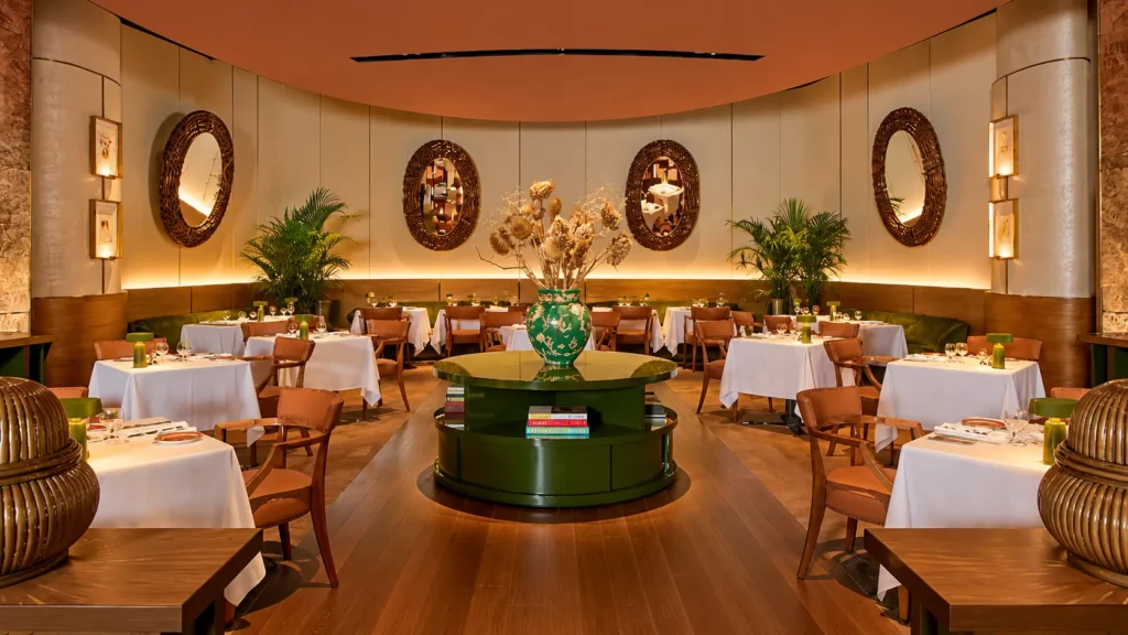 Elegant restaurant dining room with round tables, cream chairs, decorative wall mirrors and a green centerpiece