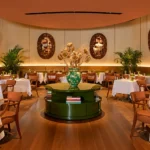 Elegant restaurant dining room with round tables, cream chairs, decorative wall mirrors and a green centerpiece