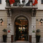 Historic stone entrance with a decorative arch and red awnings at Four Seasons Hotel Milano