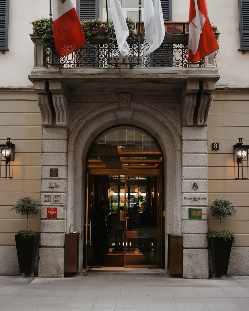 Historic stone entrance with a decorative arch and red awnings at Four Seasons Hotel Milano