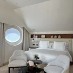 Elegant hotel bedroom with white linens, contemporary furnishings and a circular window at Four Seasons Hotel Milano