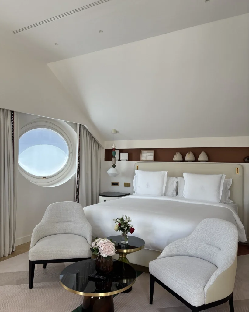 Elegant hotel bedroom with white linens, contemporary furnishings and a circular window at Four Seasons Hotel Milano