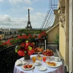 Breakfast table with flowers and pastries on a private balcony overlooking the Eiffel Tower at Hôtel Plaza Athénée Paris