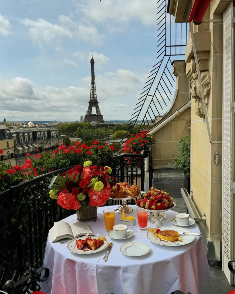 Breakfast table with flowers and pastries on a private balcony overlooking the Eiffel Tower at Hôtel Plaza Athénée Paris