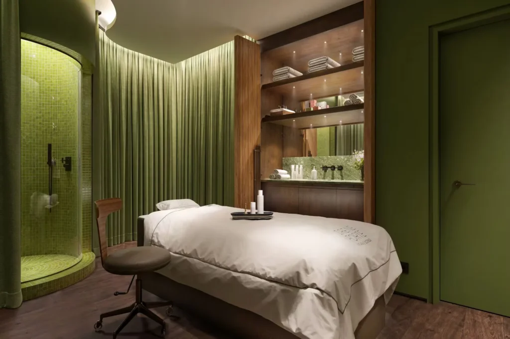 Irene Forte Spa treatment room at The Carlton Milan featuring a massage bed, green-toned walls, soft lighting, and natural textures