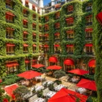 Hôtel Plaza Athénée Paris courtyard restaurant with lush ivy-covered walls, red umbrellas and elegant outdoor dining tables