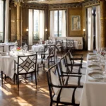 Elegant Parisian dining salon with ornate walls, chandeliers and beautifully set tables at La Réserve Paris
