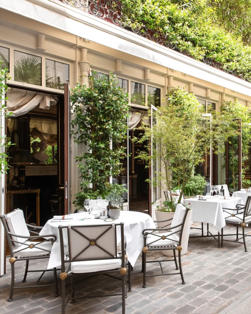 Bright garden restaurant terrace with white tables and greenery at La Réserve Paris