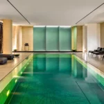 Symmetrical indoor spa pool with turquoise water, stone walls and contemporary lounge seating