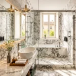 Bright marble bathroom with a freestanding bathtub, gold fixtures, glass shower and natural light from tall windows