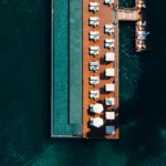 Aerial view of a long overwater resort pool surrounded by deep blue ocean and rows of lounge seating
