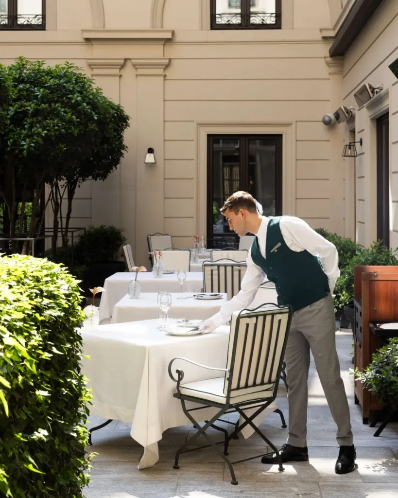 Outdoor dining table prepared with white linens and elegant tableware in the landscaped courtyard of Mandarin Oriental Milan