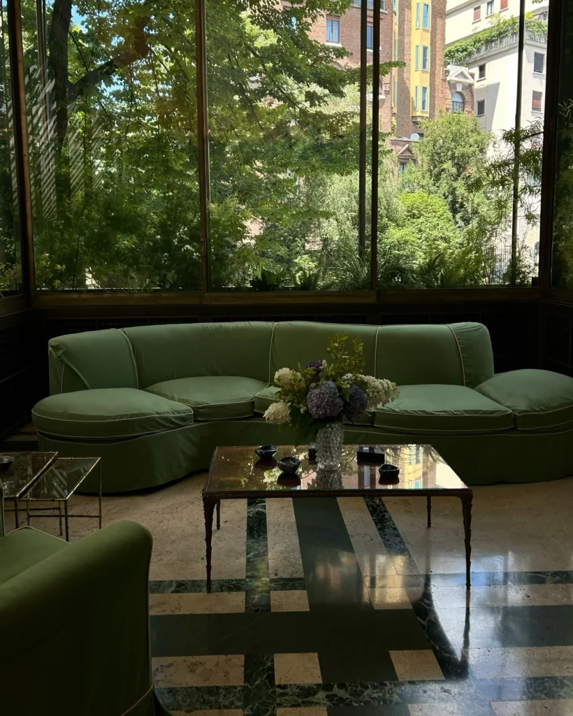 Contemporary lounge with deep green sofas, a glass coffee table and floor-to-ceiling windows overlooking greenery at Mandarin Oriental Milan