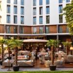 Contemporary hotel courtyard with outdoor lounge seating, greenery and a refined building facade