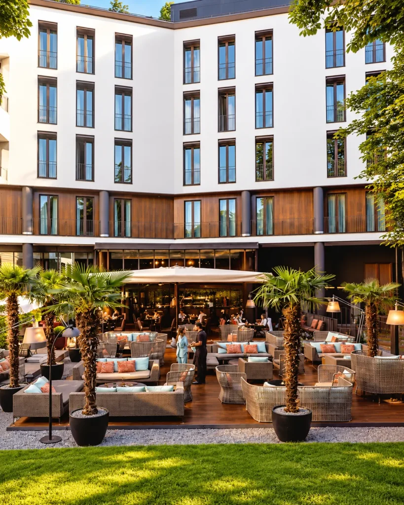 Contemporary hotel courtyard with outdoor lounge seating, greenery and a refined building facade