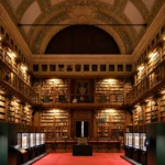 Grand historic library with symmetrical bookshelves, an ornate arched ceiling and a central red carpet