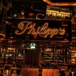 Philipp's luxury restaurant interior featuring an illuminated sign, amber lighting, mirrored walls, and elegant dining tables.