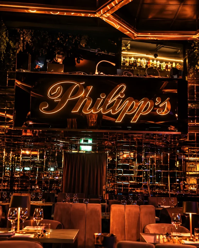Philipp's luxury restaurant interior featuring an illuminated sign, amber lighting, mirrored walls, and elegant dining tables.