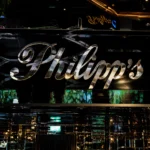 Philipp's luxury restaurant featuring a polished metallic sign, mirrored walls, elegant black interiors, and ambient golden lighting.