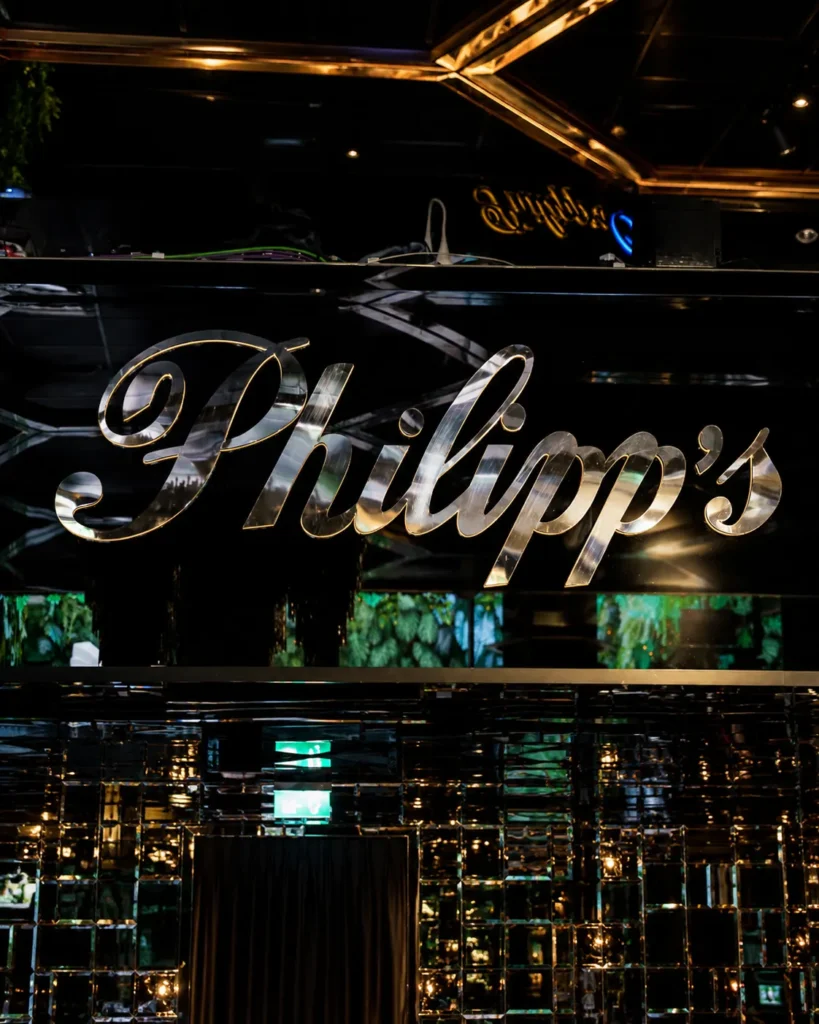 Philipp's luxury restaurant featuring a polished metallic sign, mirrored walls, elegant black interiors, and ambient golden lighting.