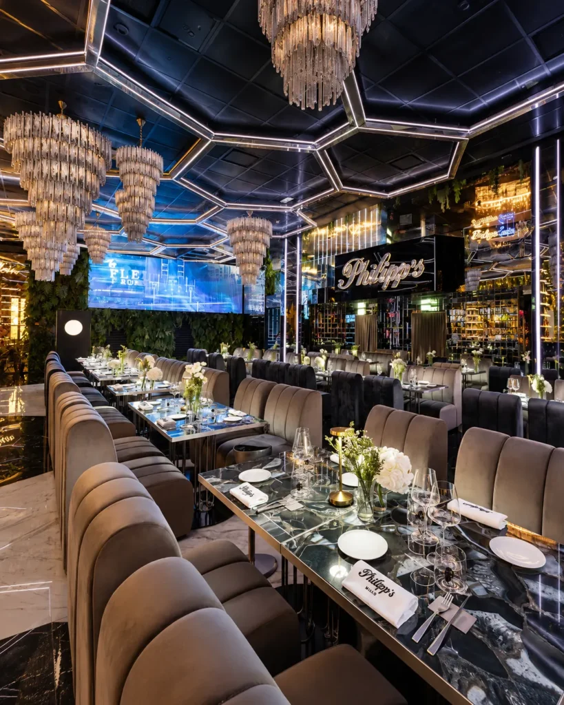 Philipp's elegant restaurant interior featuring geometric ceiling lights, crystal chandeliers, mirrored walls, marble dining tables, and plush velvet seating.