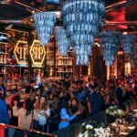 Elegant nightclub dining area with a large crystal chandelier, colorful lighting and guests at Philipp's Club Milano