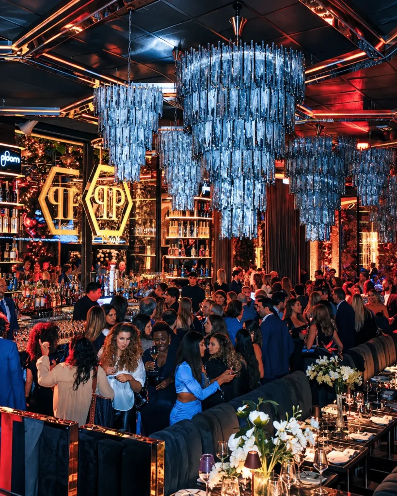 Elegant nightclub dining area with a large crystal chandelier, colorful lighting and guests at Philipp's Club Milano